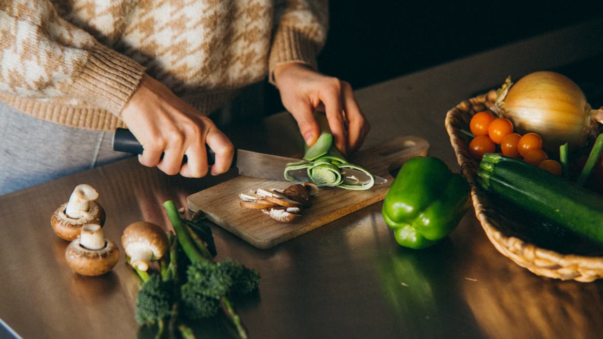 Close-up of hands slicing fresh vegetables on a wooden board in the kitchen.